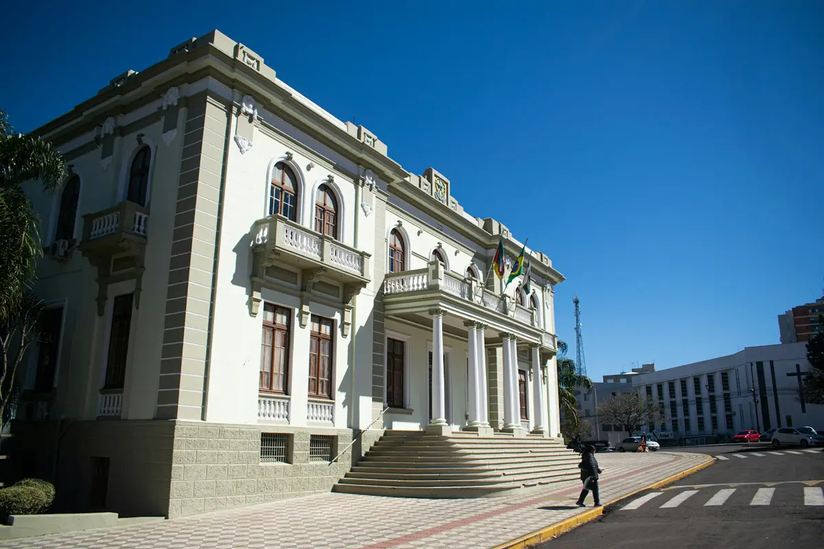 Prédio público antigo, branco, com escadaria e sacadas, numa esquina de cidade
