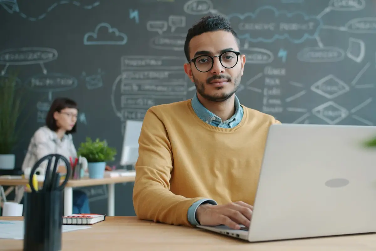 Homem de óculos trabalha num notebook numa mesa de escritório