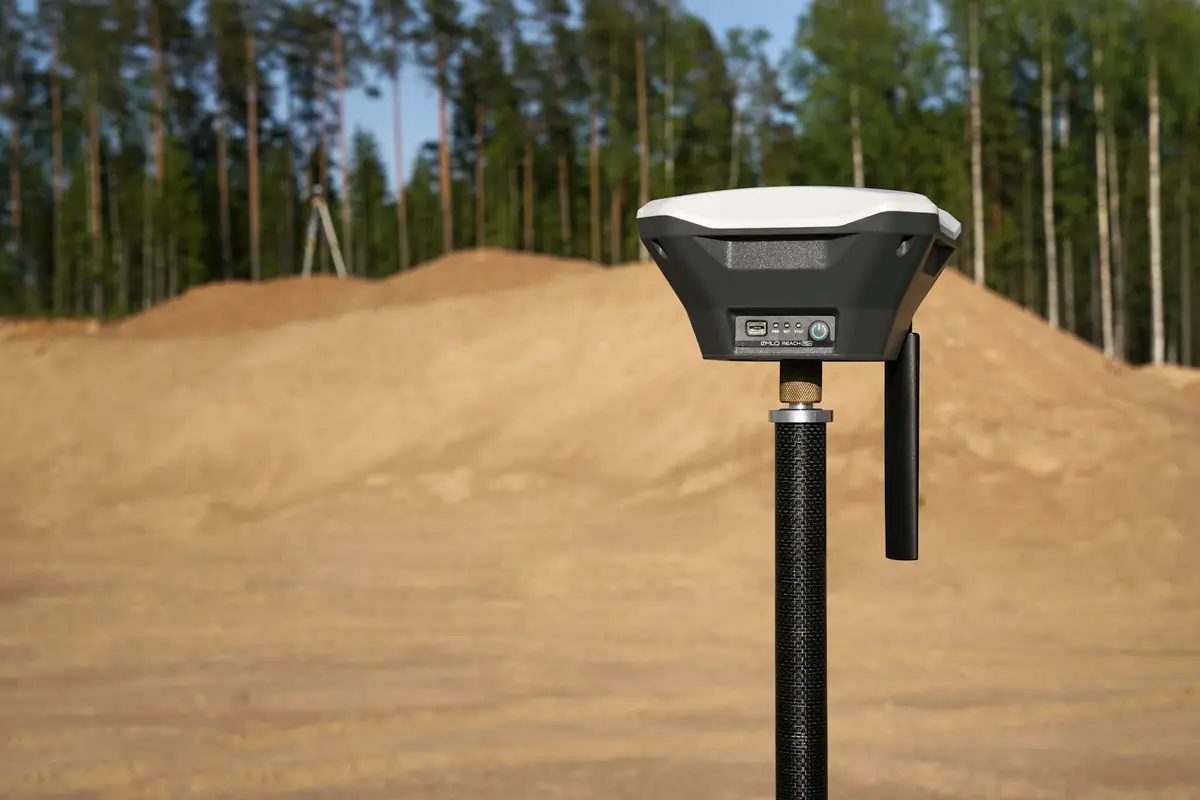 Receptor GNSS branco e preto montado num bastão, em terreno de terra batida