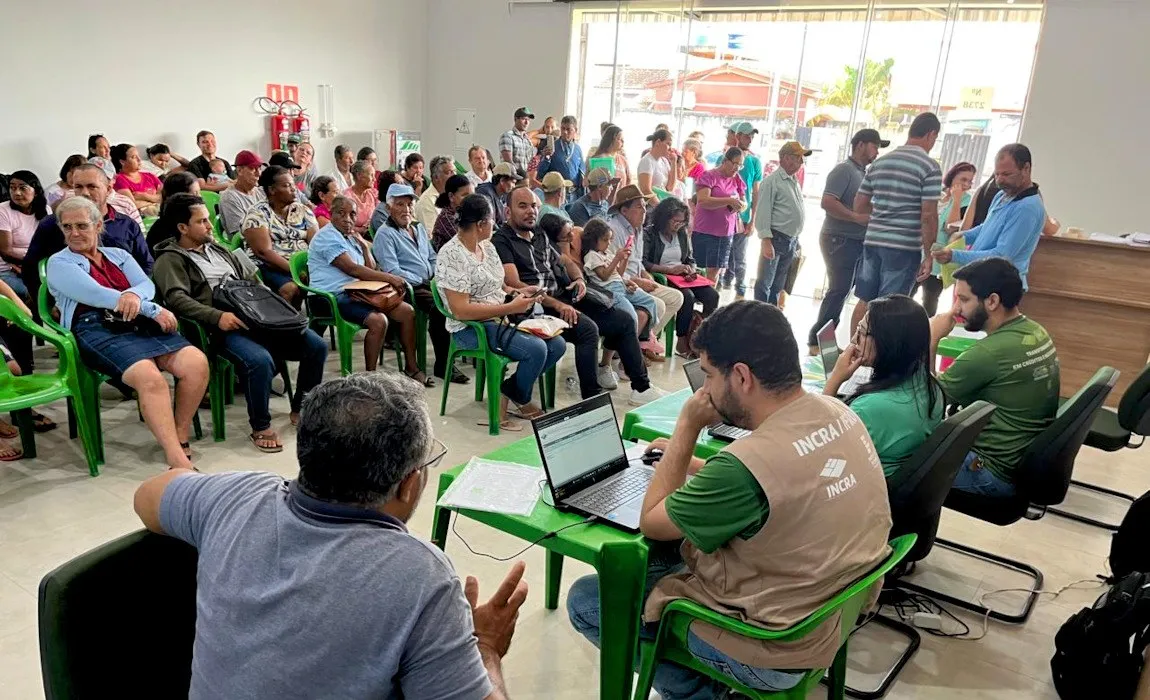 Servidor do Incra atende numa mesa com notebook, diante de uma sala cheia de produtores rurais esperando