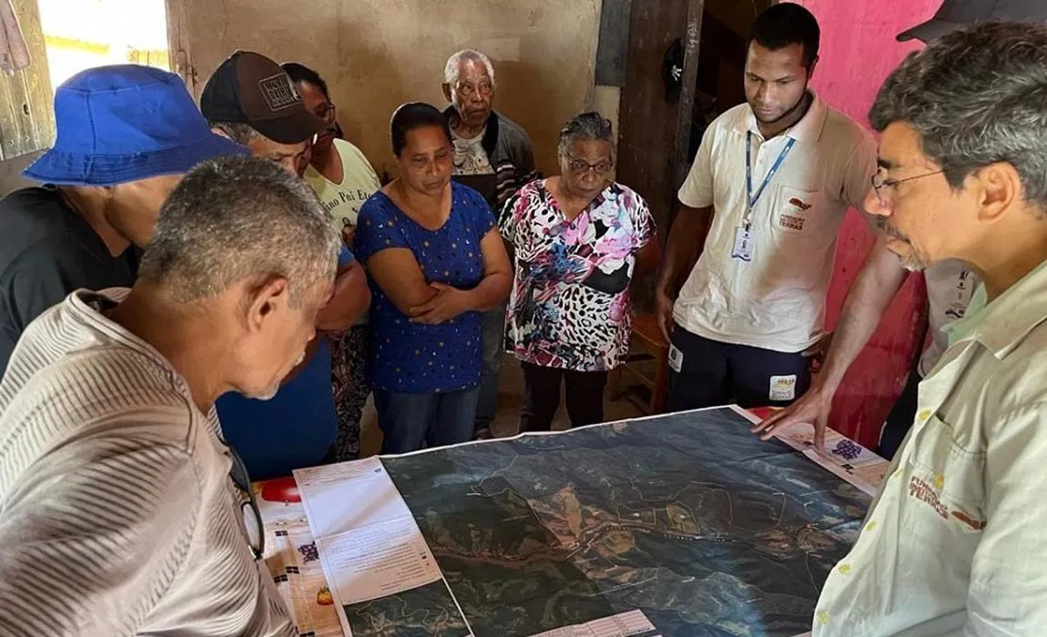 Técnicos e moradores em volta de uma mesa olham um mapa impresso, com imagem de satélite e os limites da área