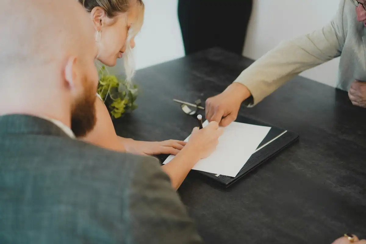 Pessoas assinando um documento numa mesa, com alguém mostrando onde assinar