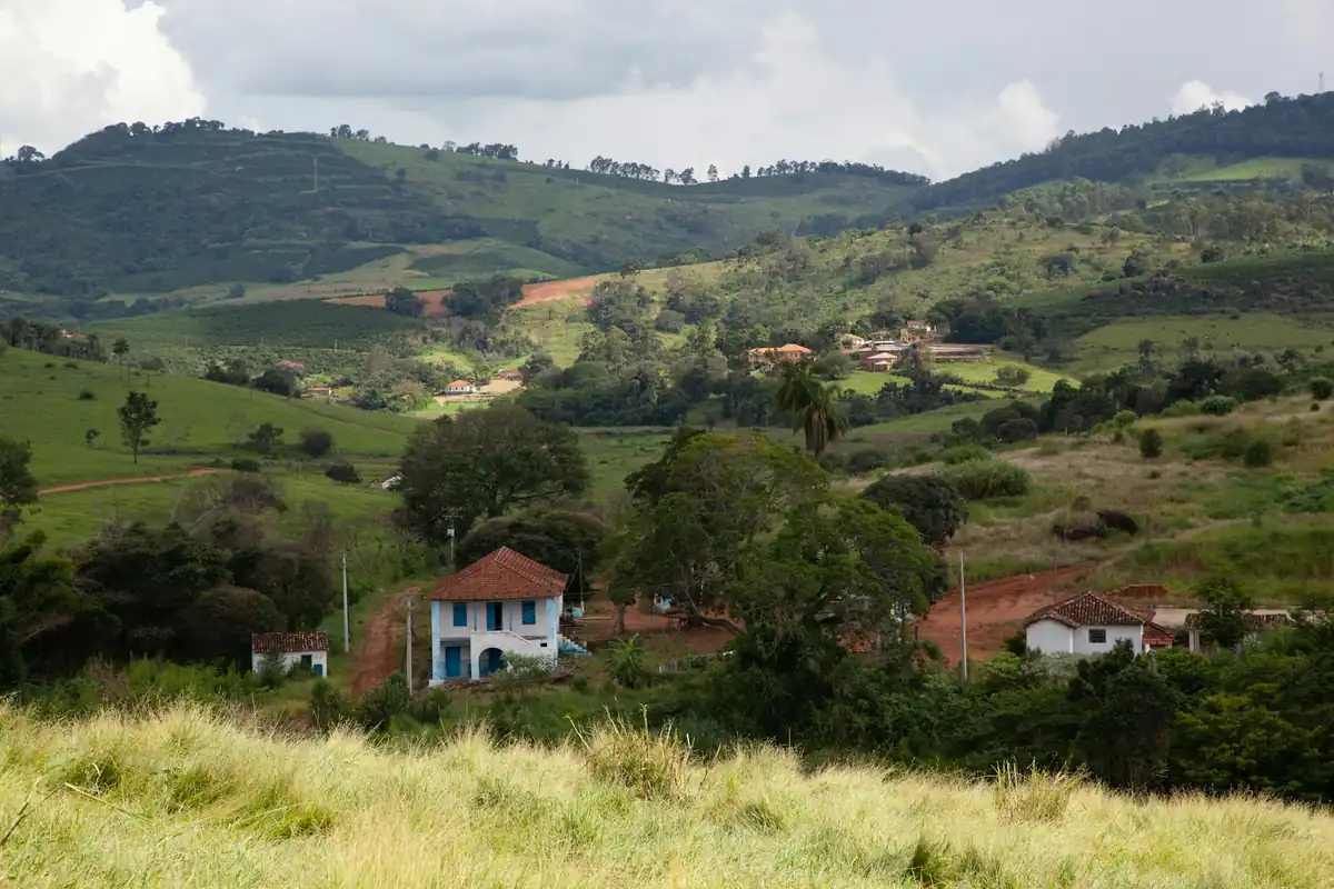 Casa de fazenda com telhado de barro entre morros, pastos e estradas de terra