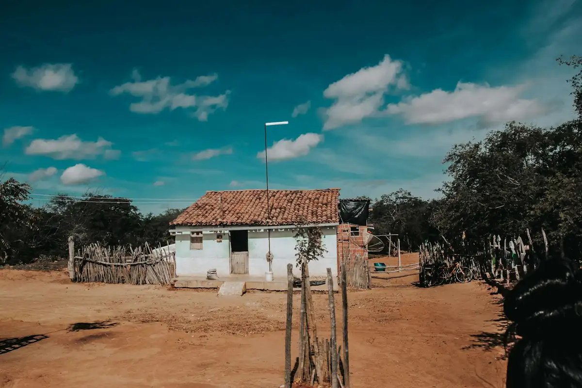 Casa simples de telhado de barro com cerca de varas no terreiro de terra